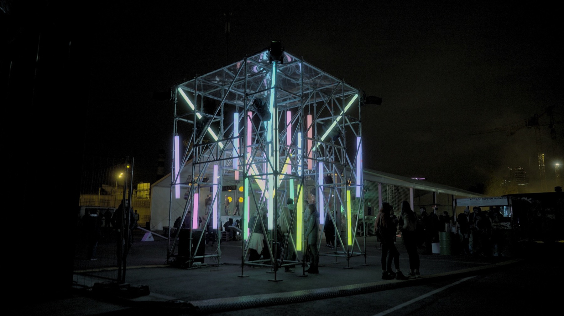 Wide night view of POKE-N-CLICK with illuminated aluminium frame and visitors