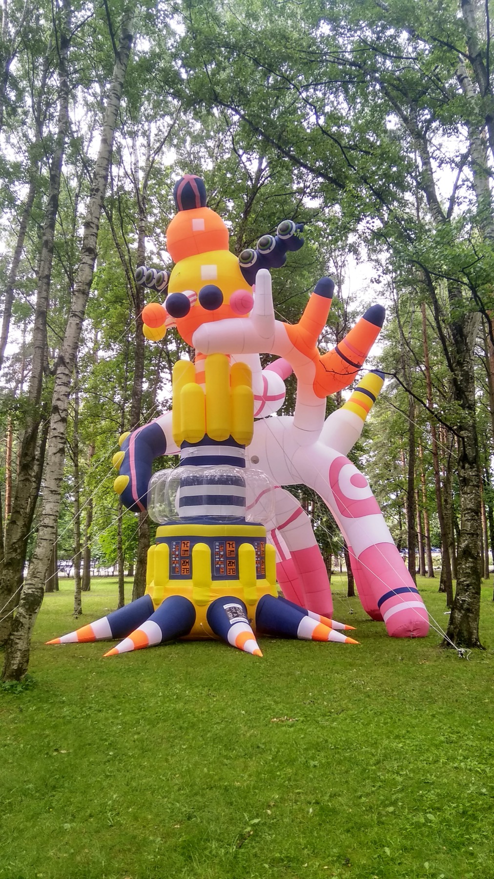 Front view of RazDva, a tall colorful inflatable sculpture in a wooded park