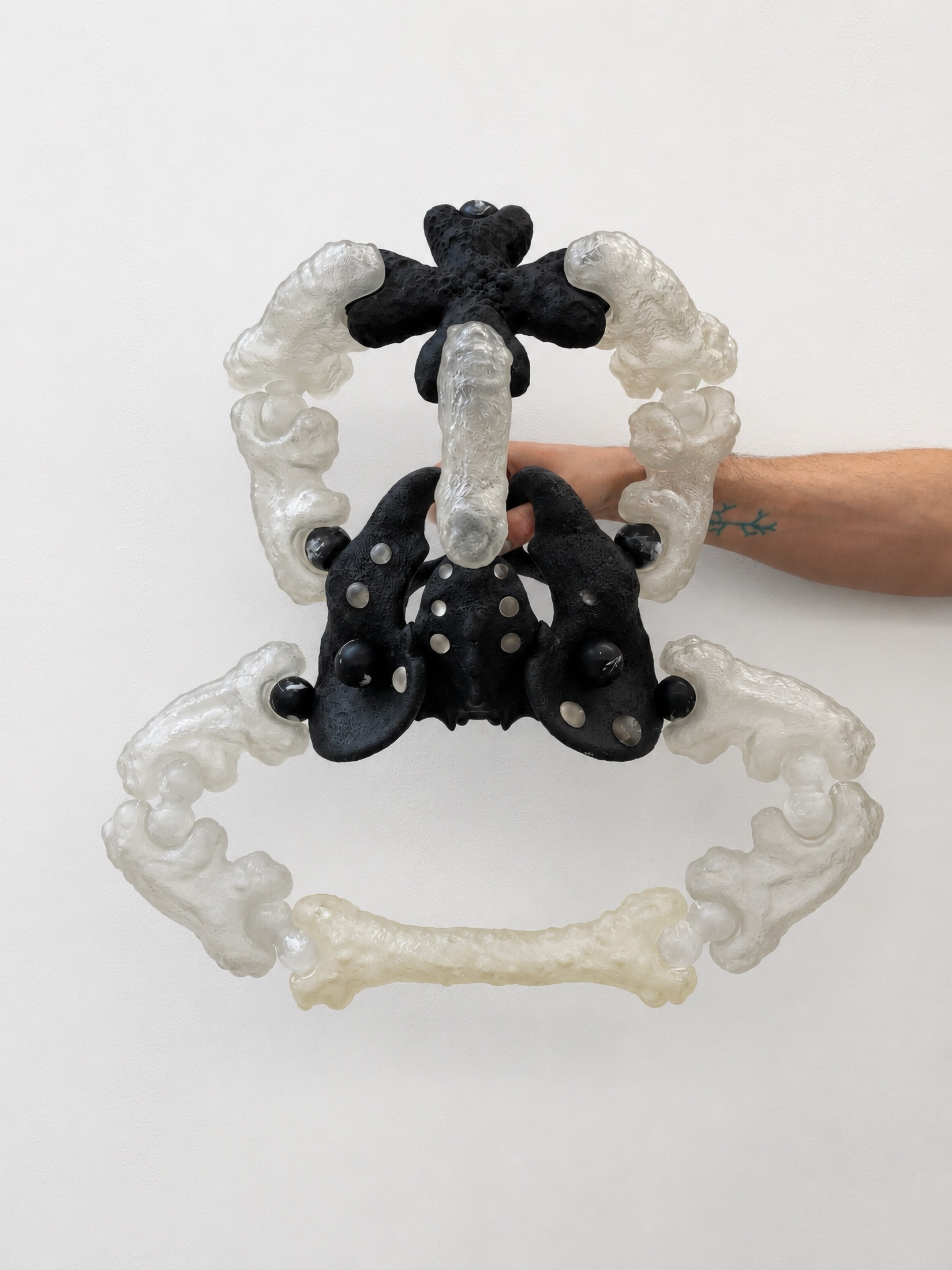 Hand holding a black and translucent Rebone organizm'os circular structure against a white wall