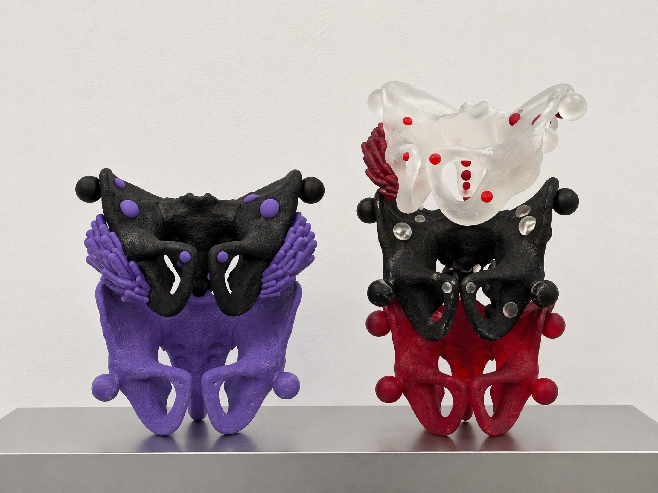 Two Rebone organizm'os pelvis-like structures in purple, black, red, and translucent resin on a metal surface