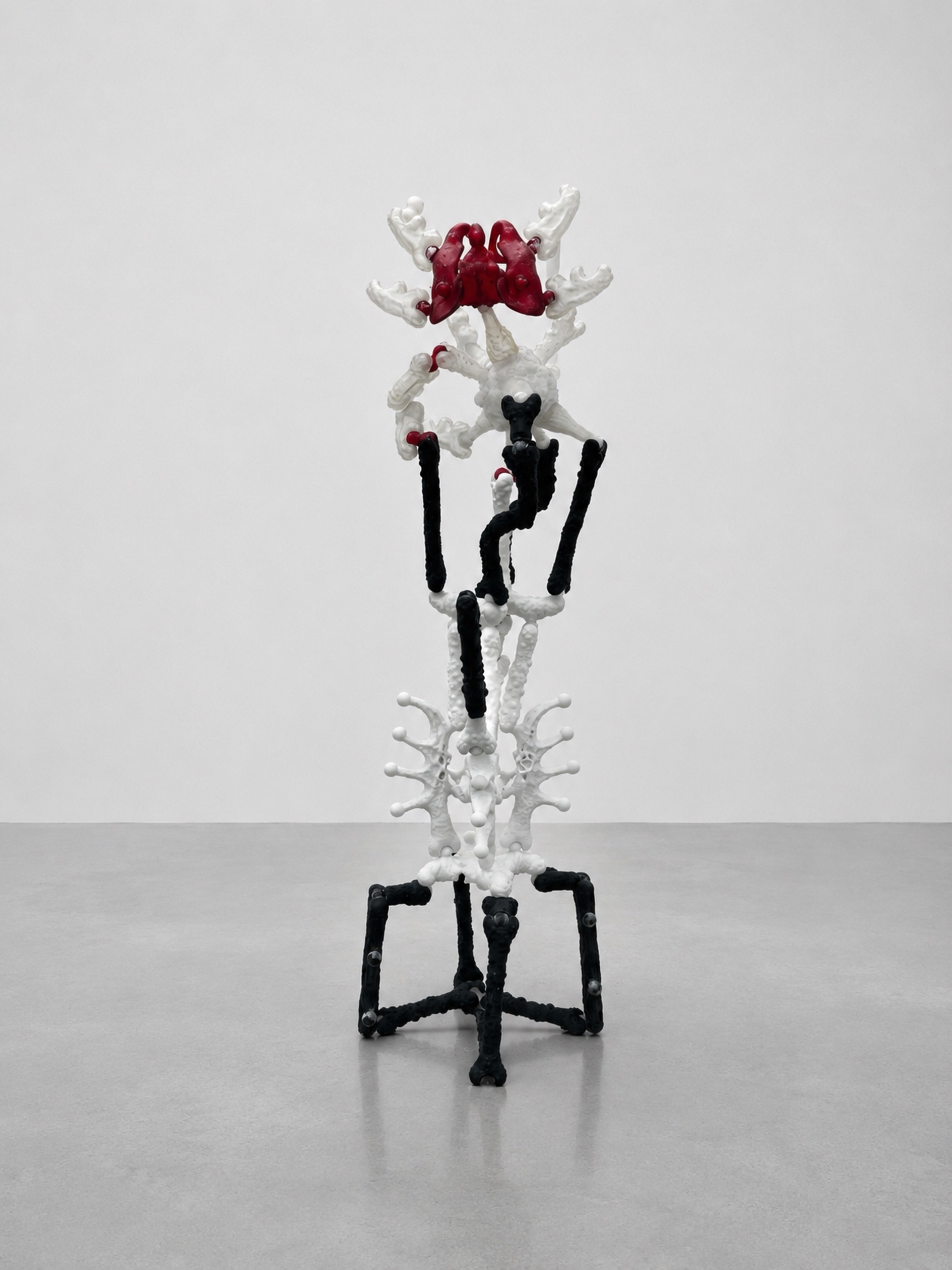 Tall white, black, and red Rebone organizm'os standing structure against a white gallery wall