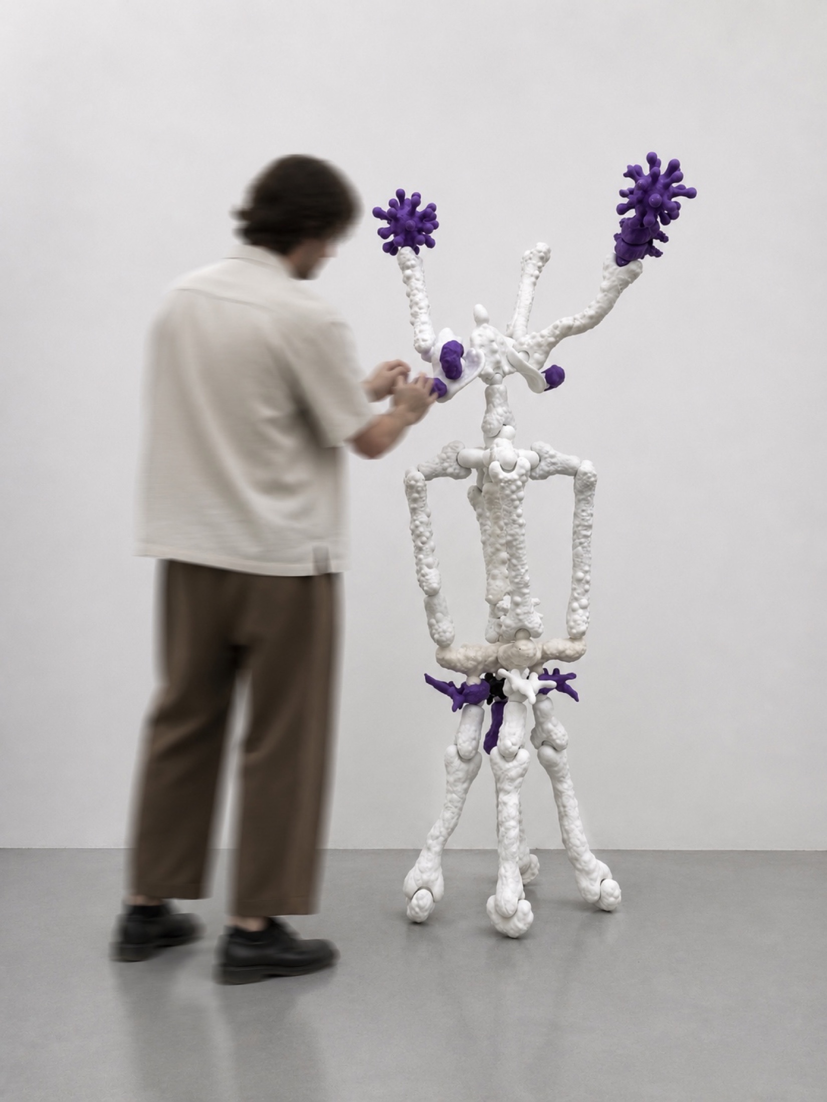 Visitor adjusting a white and purple Rebone organizm'os standing organism in the gallery