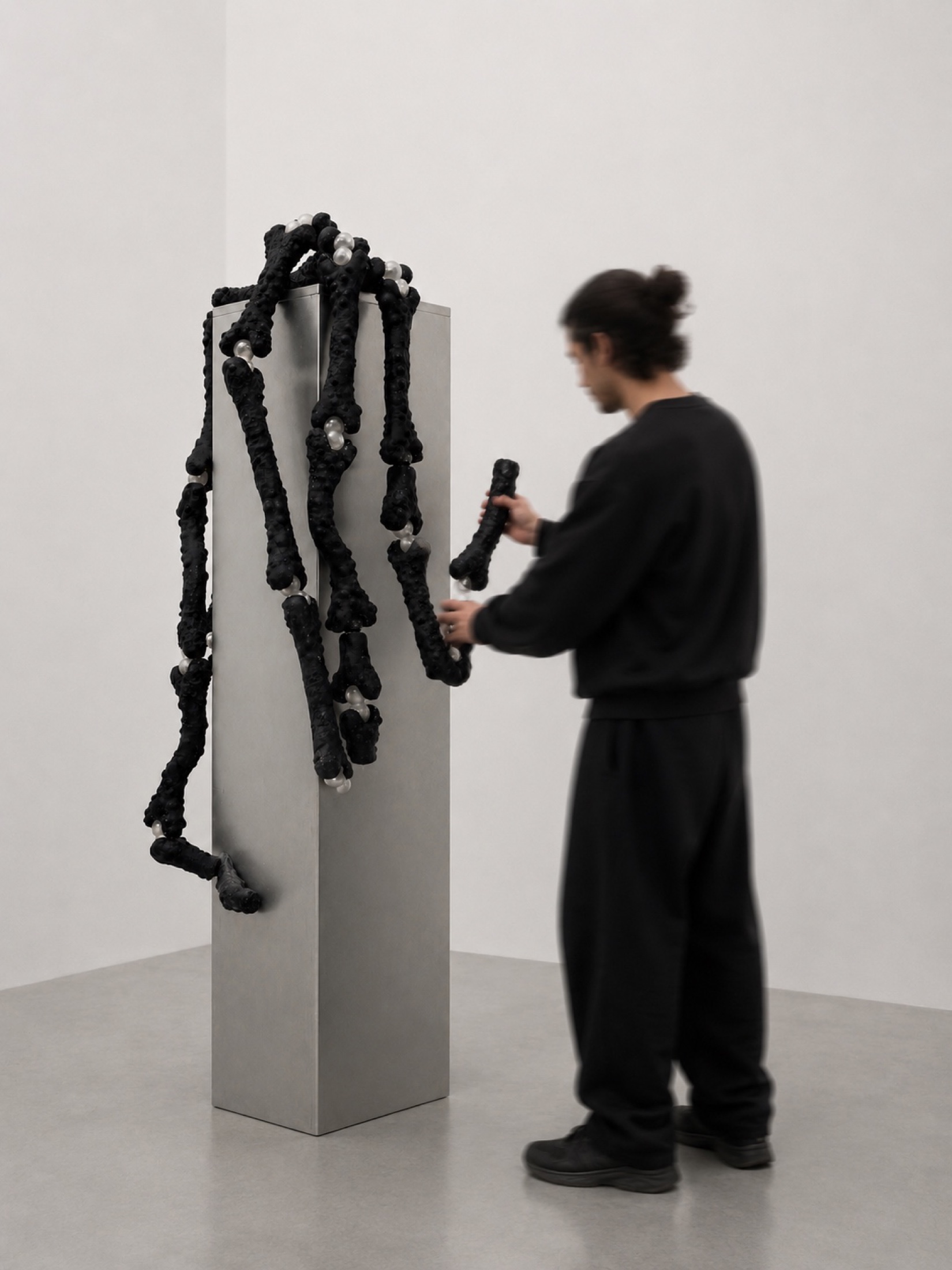 Visitor working near a black Rebone organizm’os assemblage on a metal plinth